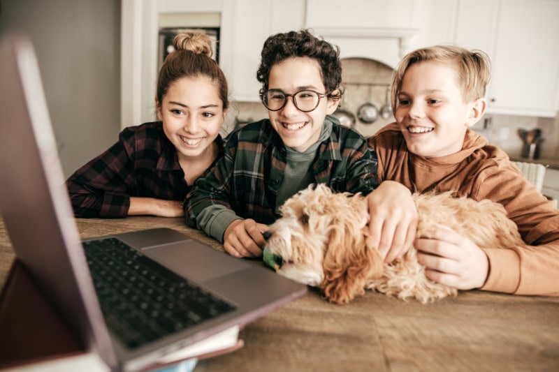teens sitting at a table smiling at a laptop together.