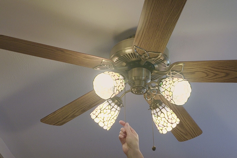 Person turning on their ceiling fan in order to save energy|